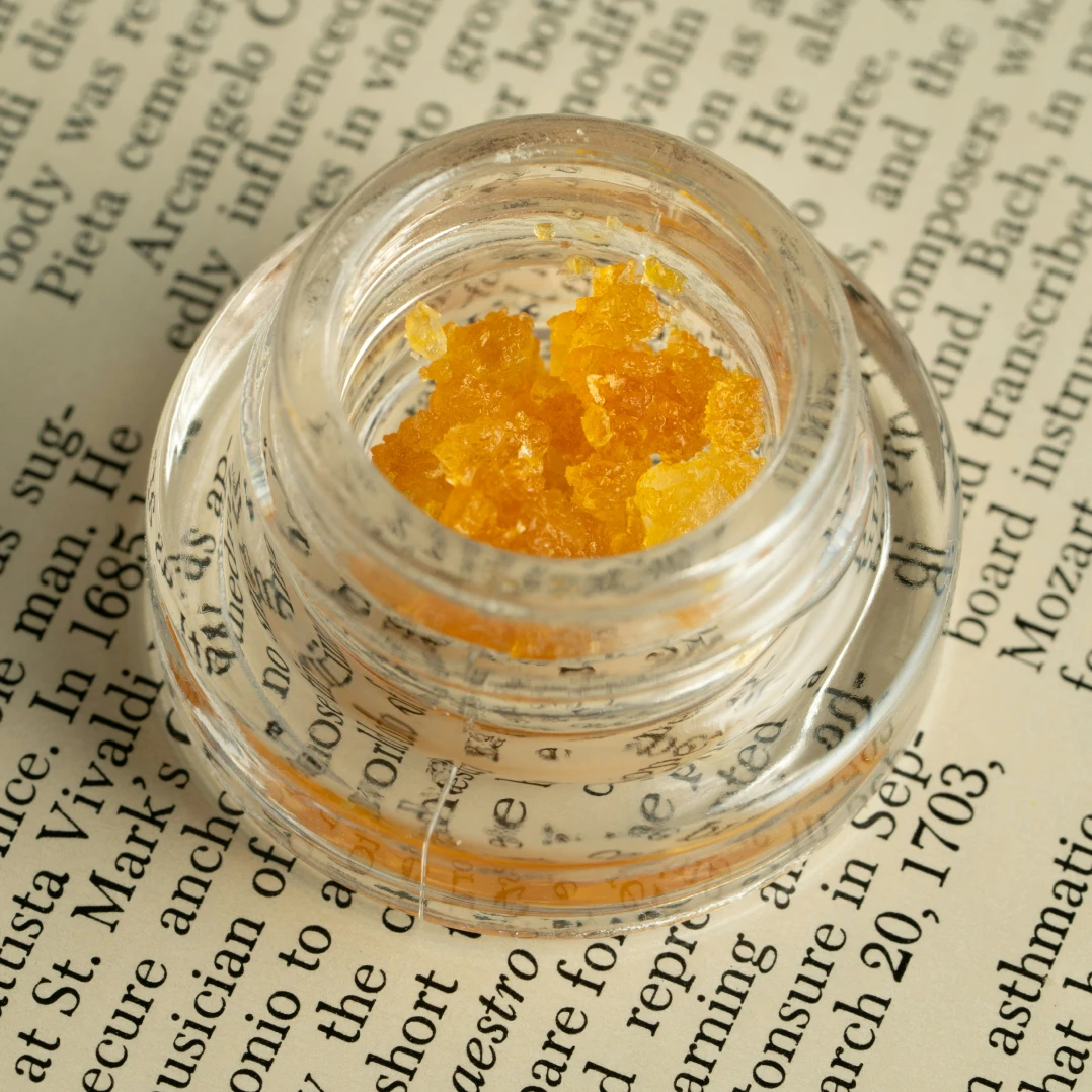 A glass dabbing container filled with golden, crystalline THCA concentrate, showcasing its rich texture and purity.